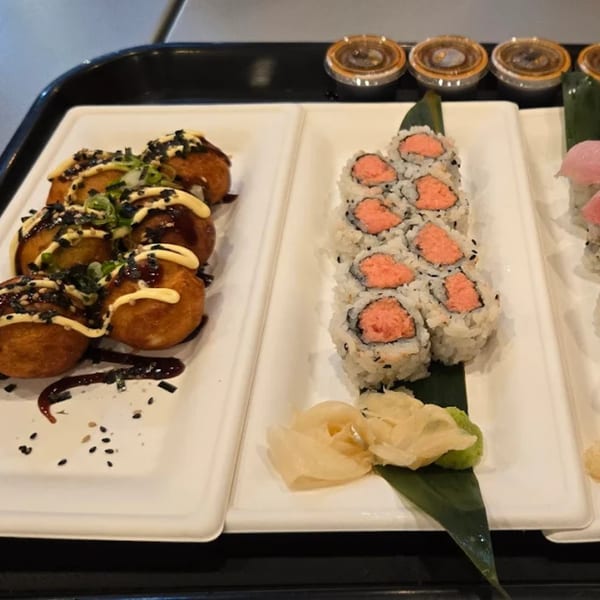 Plates of takoyaki drizzled with sauce and tuna sushi rolls with ginger and wasabi.
