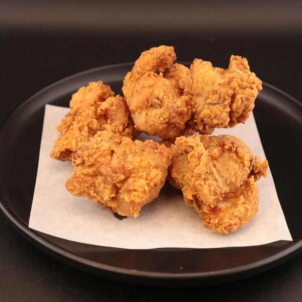 Five pieces of crispy fried chicken on white parchment paper on a black plate.