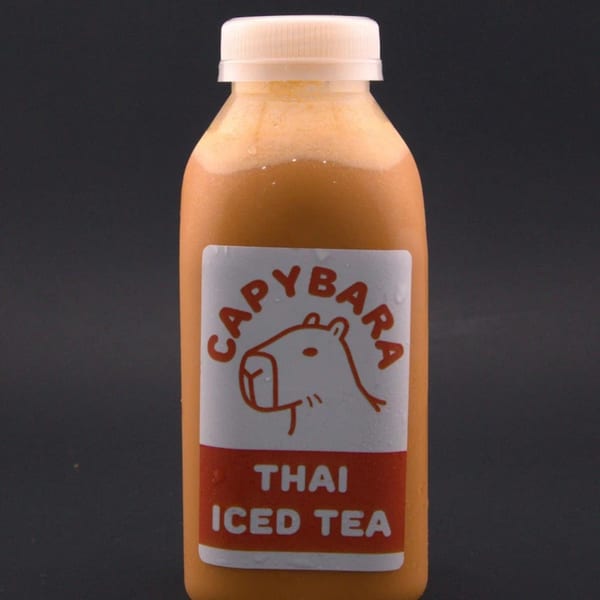 A bottle of Capybara Thai Iced Tea with a white cap on a dark background.
