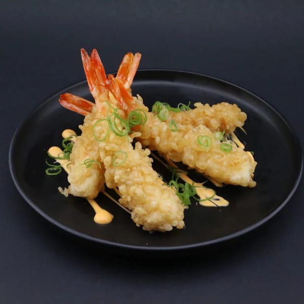 Three crispy tempura shrimp with orange tails, drizzled with sauce and garnished with green onions.