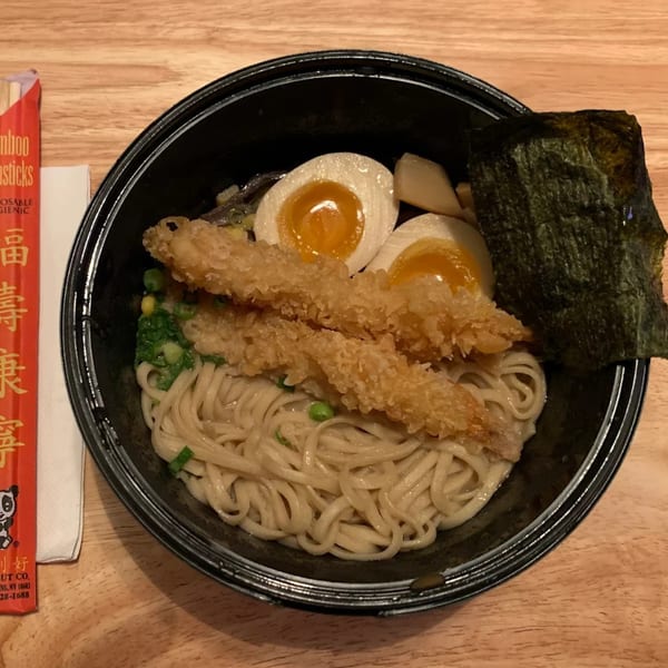 Ramen bowl with noodles, two fried shrimp, two soft-boiled eggs, and nori on a wooden table.