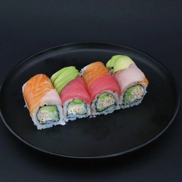 Rainbow sushi roll with salmon, tuna, and avocado on a black plate.