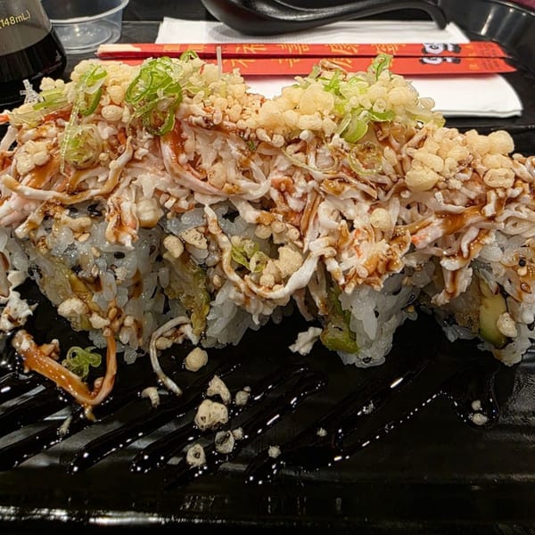 Sushi rolls topped with shredded crab, crispy tempura flakes, green onions, and a drizzle of sauce.